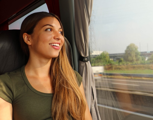 Foto mujer hermosa joven que mira por la ventana del autobús. pasajero de autobús feliz viajando sentado en un asiento y mirando por la ventana.