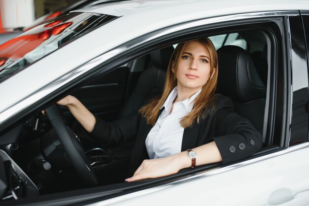 Mujer hermosa joven que muestra su amor a un coche en una sala de exposición de coches