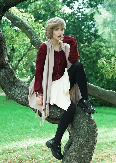 Mujer hermosa joven que presenta en un árbol. Retrato de moda glamour. Parque de otoño.