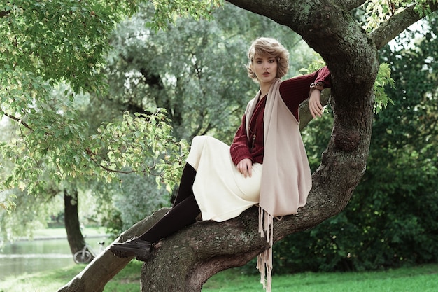 Mujer hermosa joven que presenta en un árbol. Retrato de moda glamour. Parque de otoño.