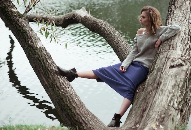 Mujer hermosa joven que presenta en un árbol. Retrato de moda glamour. Parque de otoño.