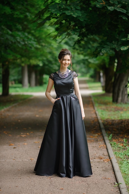 Mujer hermosa joven que presenta en un vestido negro en un parque.