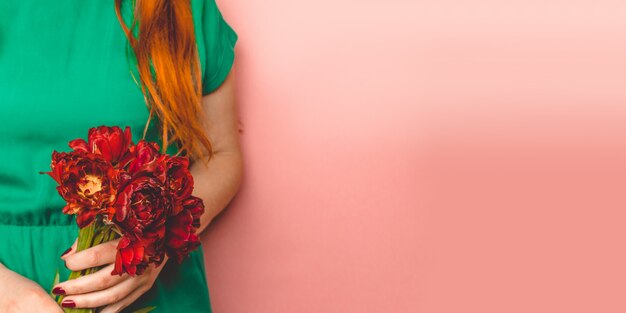 Mujer hermosa joven que sostiene un ramo de la primavera de tulipanes rojos en su mano.