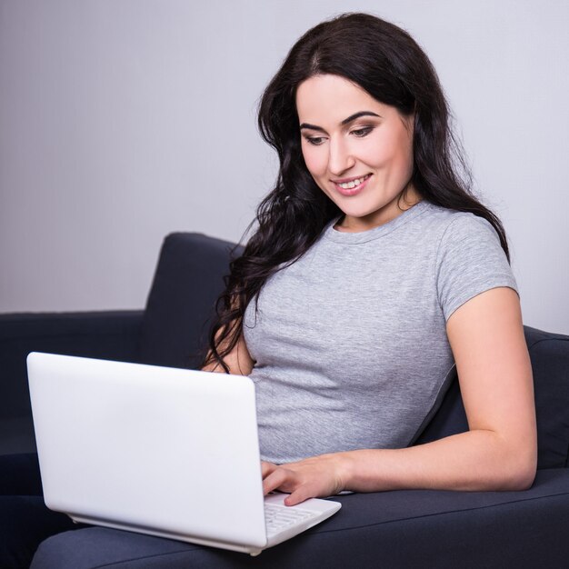 Mujer hermosa joven que usa la computadora en casa