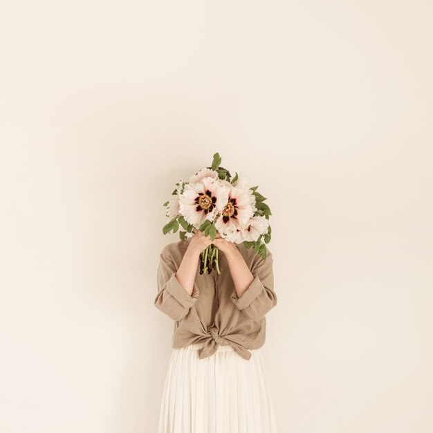 Mujer hermosa joven con ramo de flores de peonías blancas en la pared blanca