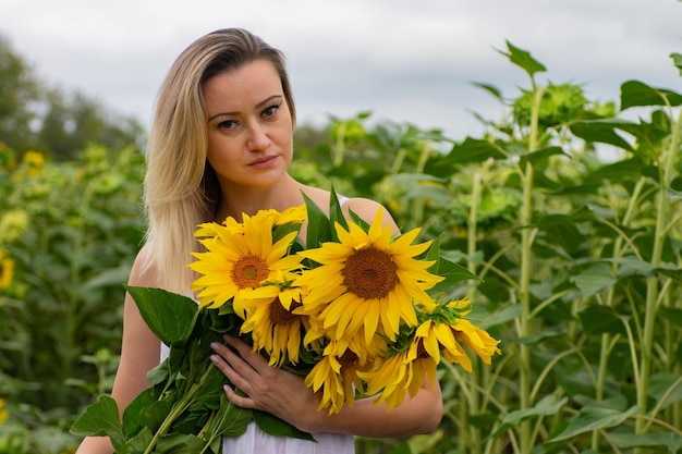 Mujer hermosa joven con un ramo de girasoles en un campo de girasoles