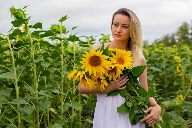 Mujer hermosa joven con un ramo de girasoles en un campo de girasoles