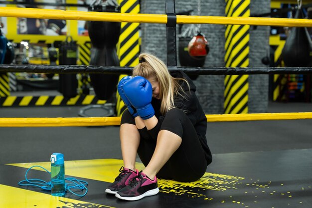 Mujer hermosa joven se relaja después de una pelea o sesión de entrenamiento y llora cubriendo su rostro