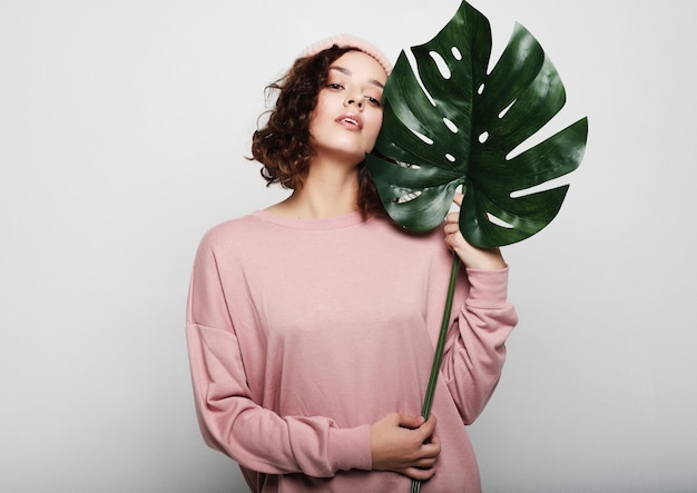 Mujer hermosa joven con ropa casual rosa con hoja de monstera