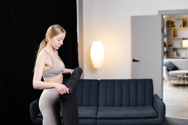 Mujer hermosa joven con ropa deportiva sosteniendo esterilla de yoga de pie en la habitación Formando estilo de vida de yoga