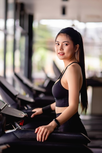 Mujer hermosa joven con ropa deportiva, tela a prueba de sudor y reloj inteligente de pie en la cinta de correr calentar antes de correr a entrenar en el gimnasio moderno