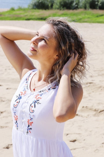 Mujer hermosa joven, rubia con cabello que se desarrolla por el viento contra la orilla arenosa. retrato.