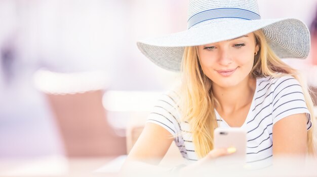 Mujer hermosa joven sentada en la cafetería y con smartphone.