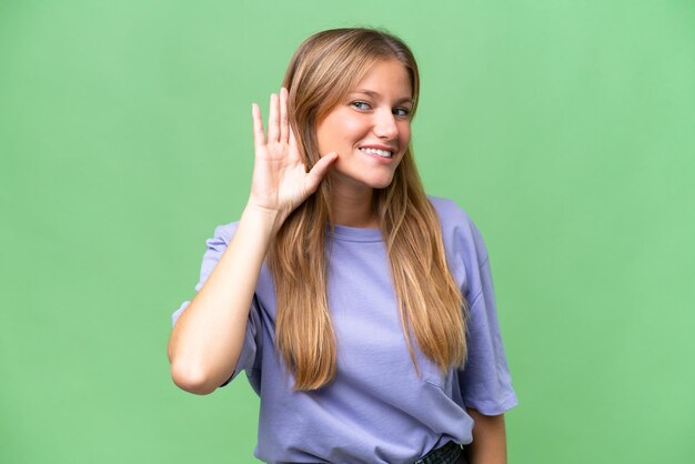 Foto mujer hermosa joven sobre un fondo aislado escuchando algo poniendo la mano en la oreja