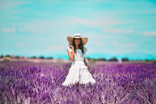 Mujer hermosa joven con sombrero blanco y vestido de pie en un campo de lavanda francés en un día soleado