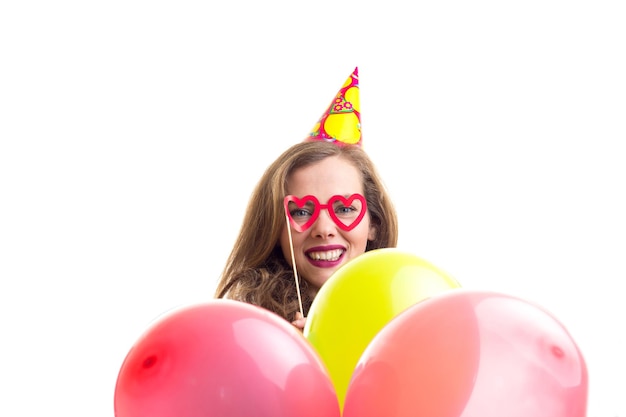 Mujer hermosa joven con sombrero de celebración sosteniendo muchos globos de colores y palo de gafas