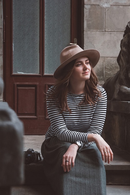 Mujer hermosa joven con sombrero está tomando fotografías con cámara antigua, al aire libre.