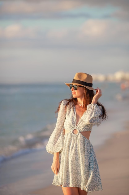 Mujer hermosa joven en sombrero de paja en la playa al atardecer