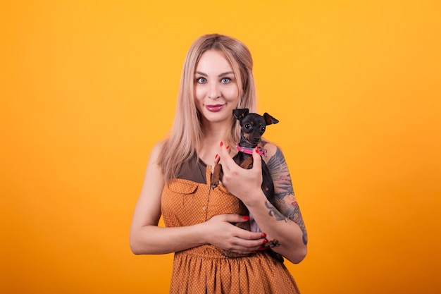 Mujer hermosa joven sonríe y abraza a su pequeño perro sobre fondo amarillo. Mujer guapa. Amor por su perro, bonito vestido.