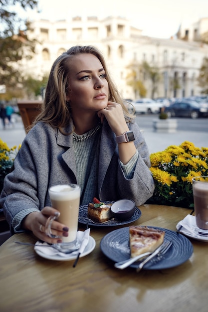 Mujer hermosa joven sonriendo y tomando café en la cafetería al aire libre de la calle