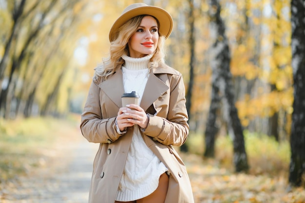 Mujer hermosa joven sosteniendo una taza con café en el parque de otoño