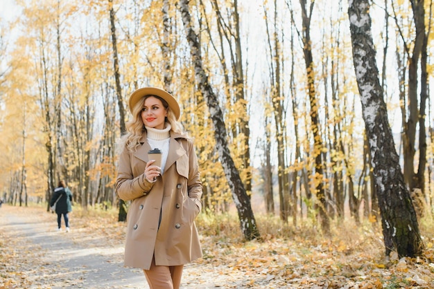 Mujer hermosa joven sosteniendo una taza con café en el parque de otoño.