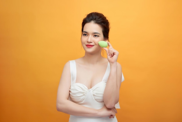 Una mujer hermosa joven sostiene una licuadora de belleza para aplicar la base de maquillaje