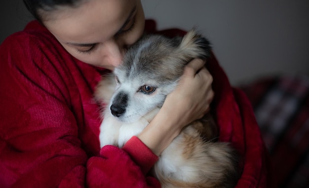 Mujer hermosa joven con su lindo perrito esponjoso en las manos en casa Concepto de mascota
