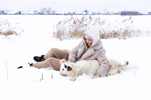 Mujer hermosa joven y su perro golden retriever divirtiéndose en invierno