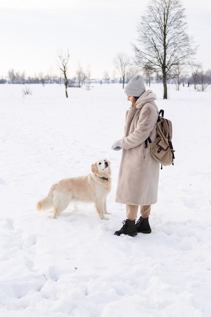 Mujer hermosa joven y su perro golden retriever divirtiéndose en invierno