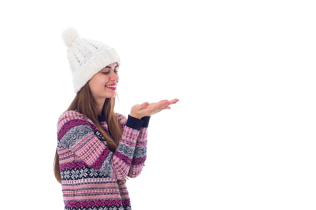 Mujer hermosa joven en suéter morado y sombrero blanco que sopla sobre fondo blanco en el estudio