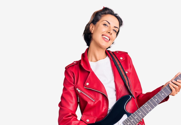 Foto mujer hermosa joven tocando la guitarra eléctrica con aspecto positivo y feliz de pie y sonriendo con una sonrisa segura mostrando los dientes