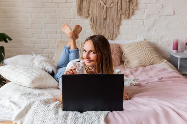 Mujer hermosa joven trabaja para una computadora portátil en la cama.