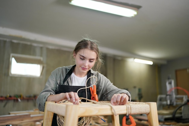 Mujer hermosa joven trabajando en la sala de taller de bricolaje de carpintero. Propietaria de una pequeña empresa, mujer joven que trabaja en una fábrica de muebles.