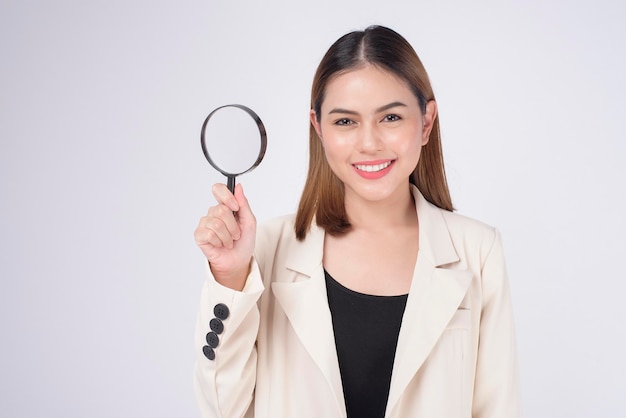 Mujer hermosa joven en traje que sostiene la lupa sobre el estudio de fondo blanco