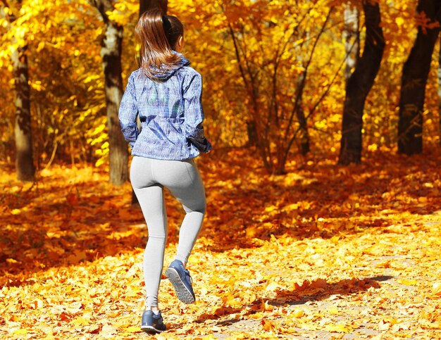 Mujer hermosa joven trotar en el parque otoño