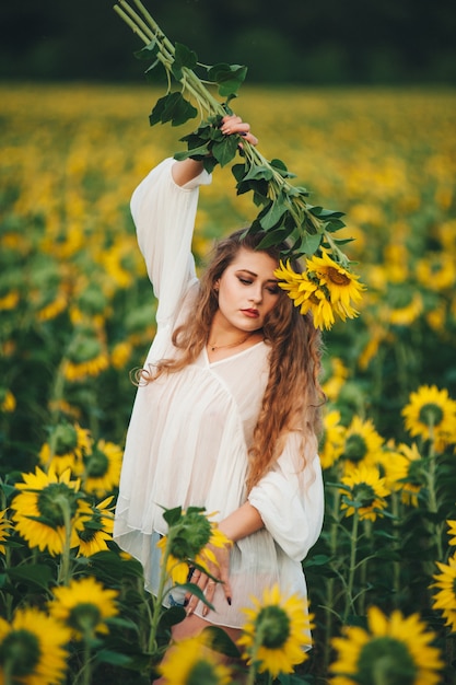 Mujer hermosa joven en un vestido entre los girasoles florecientes. Agrocultura.
