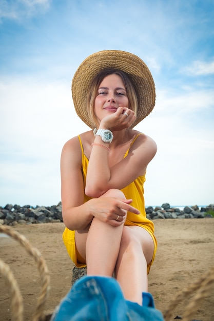 Mujer hermosa joven en un vestido informal ligero y un sombrero de paja descansando y posando sobre rocas