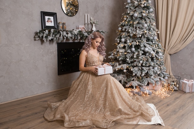 Mujer hermosa joven en vestido de noche cerca del árbol de navidad decorado