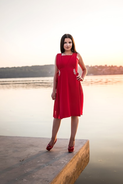 Mujer hermosa joven en vestido posando en la costa del mar al atardecer