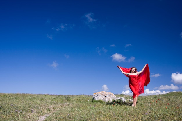 Mujer hermosa joven en vestido rojo de pie en el campo