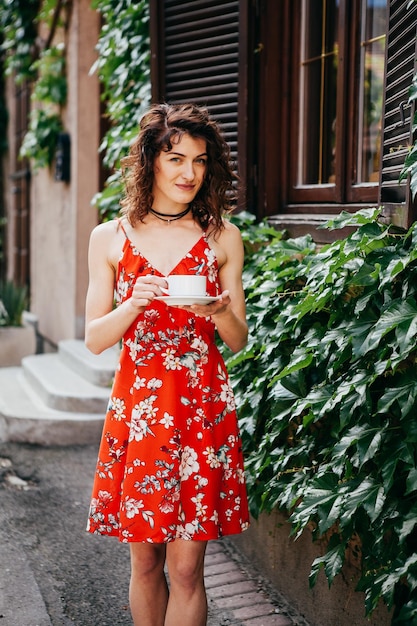 Foto mujer hermosa joven en un vestido rojo con una taza en la calle europea