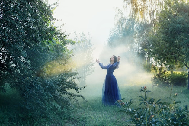 Mujer hermosa joven en vestido vintage azul en bosque mágico