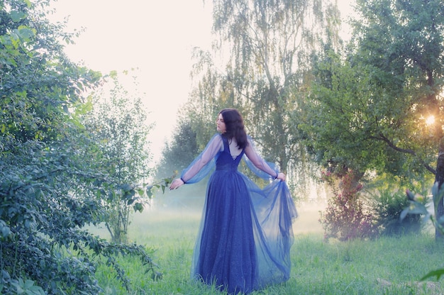 Mujer hermosa joven en vestido vintage azul en bosque mágico