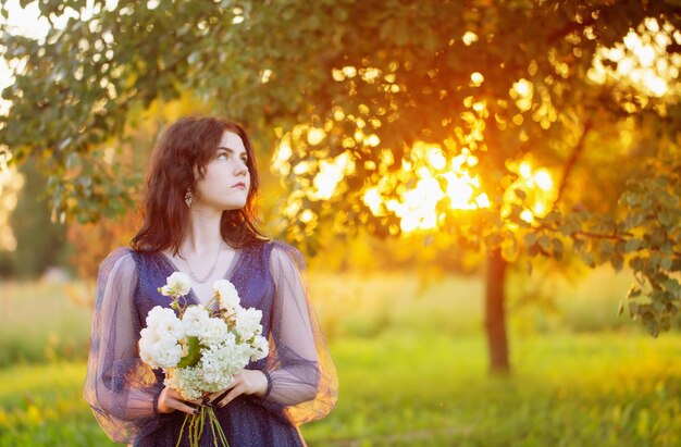 Mujer hermosa joven en vestido vintage azul con flores blancas al atardecer