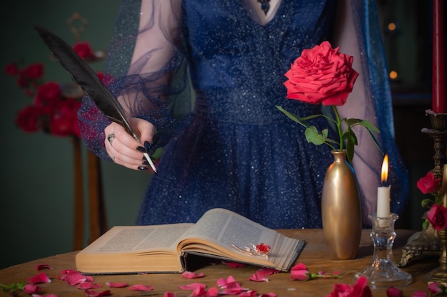 Mujer hermosa joven en vestido vintage azul con libro sobre mesa en cuarto oscuro