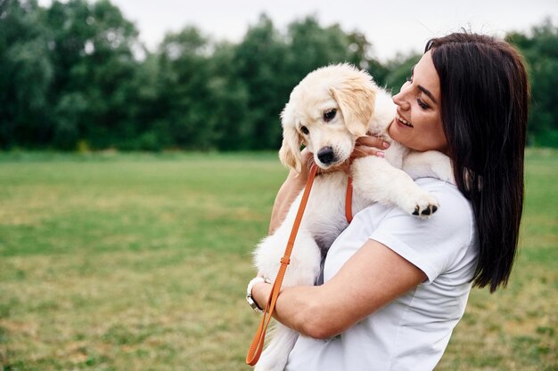 Una mujer hermosa con un lindo perro golden retriever está en el campo verde