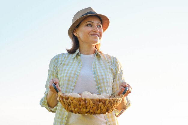 Mujer hermosa madura agricultor con canasta de huevos frescos,