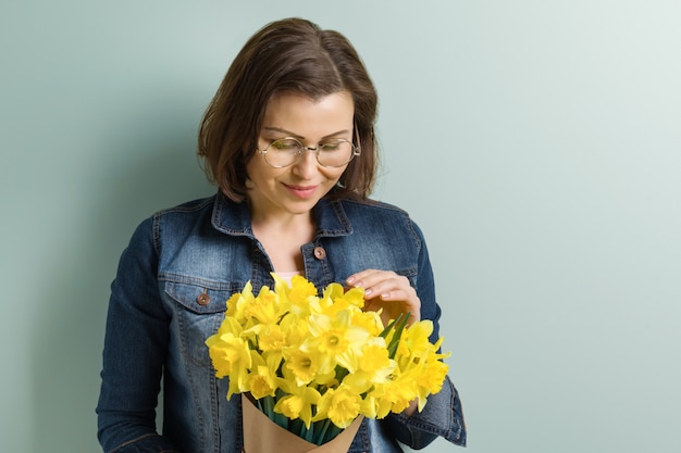 Mujer hermosa madura que sostiene el ramo de flores amarillas de la primavera