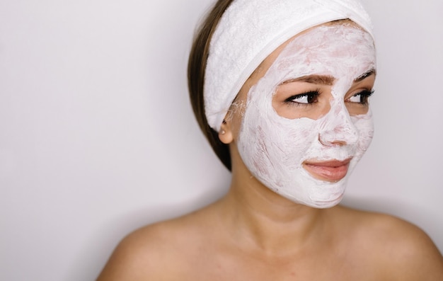 Mujer hermosa con la máscara facial en el fondo blanco